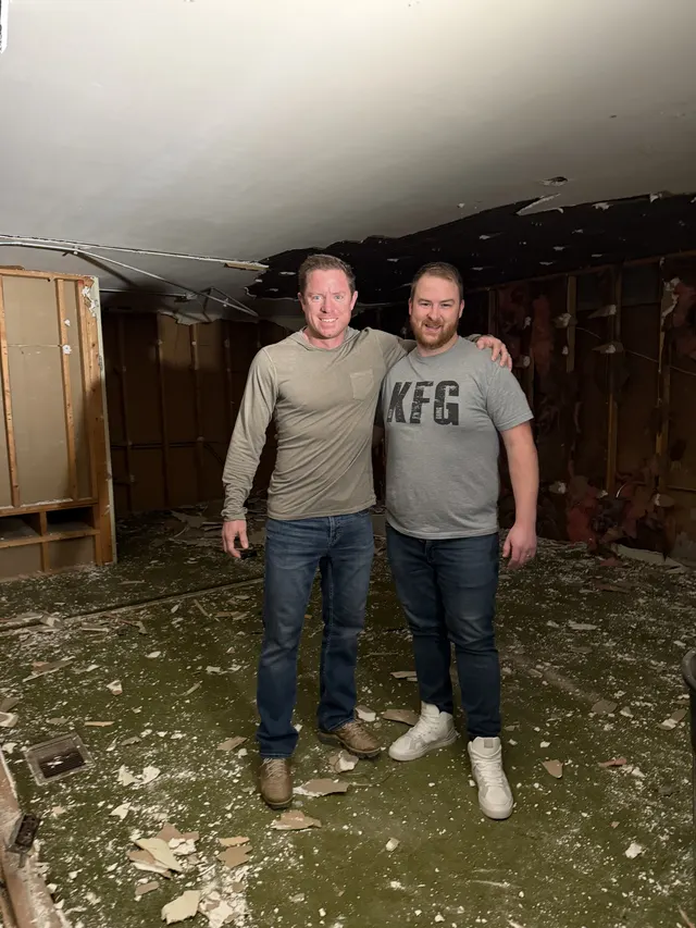 Two of the founders standing in the gutted room before the buildout, walls stripped to the studs.